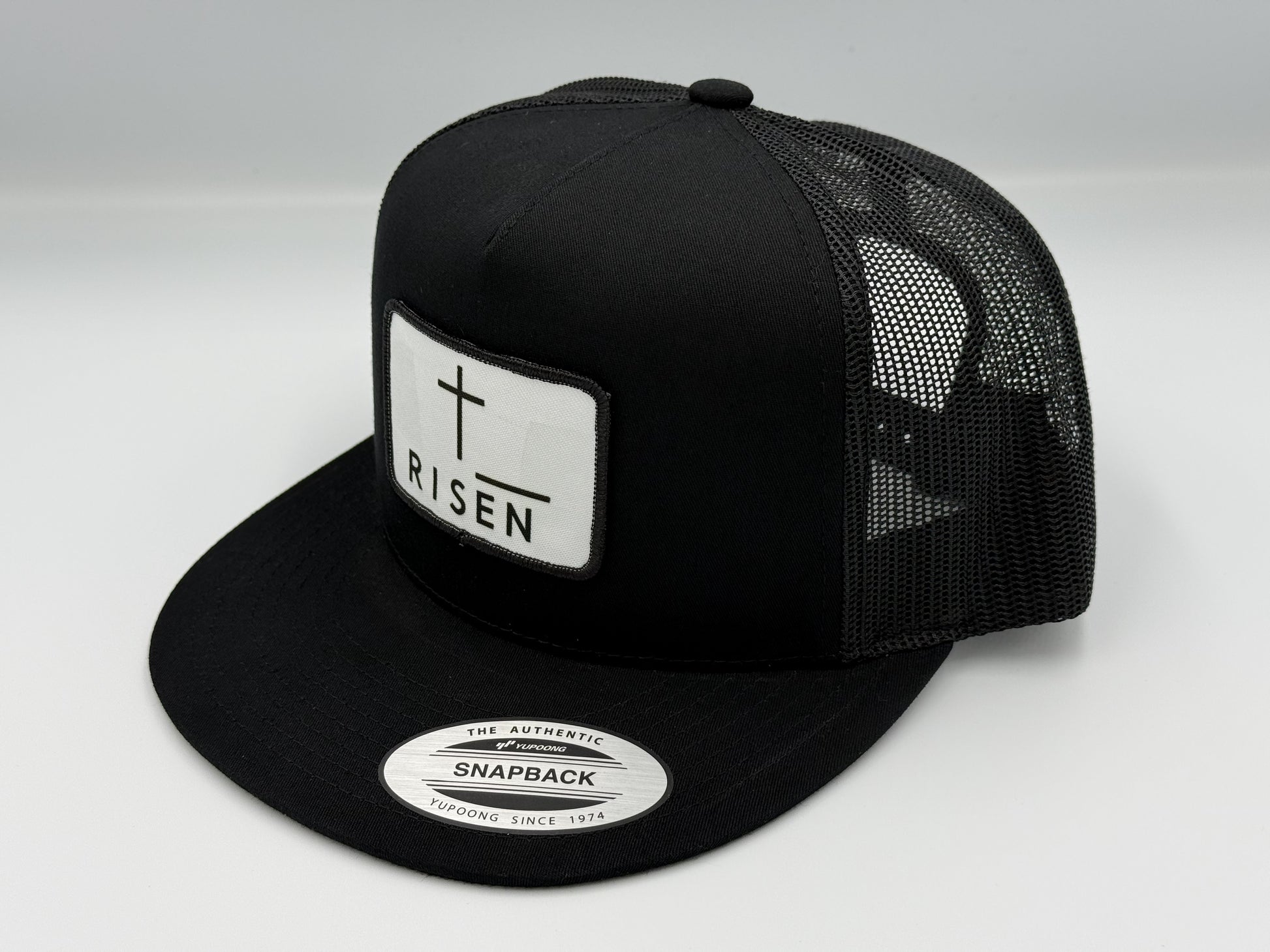 Black Trucker Snapback Hat with RISEN canvas patch and mesh back for durability and style.